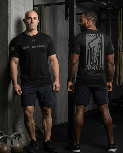 Two men modeling a black Titan 6 Endure T-shirt with the One Too Many design in a gym setting, showing the front and back views. The front of the shirt features the text 'ONE TOO MANY' in white, while the back displays a distressed American flag graphic with a fist and the text 'ONE TOO MANY' and 'IGY6'.