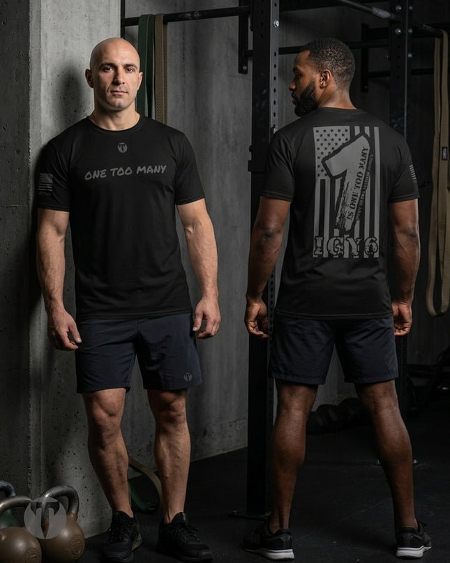Two men modeling a black Titan 6 Endure T-shirt with the One Too Many design in a gym setting, showing the front and back views. The front of the shirt features the text 'ONE TOO MANY' in white, while the back displays a distressed American flag graphic with a fist and the text 'ONE TOO MANY' and 'IGY6'.