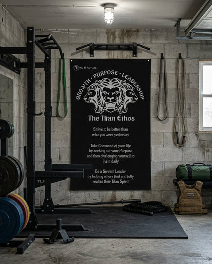 Titan 6 Actual "The Titan Ethos" Gym Banner featuring a multi-headed lion motif and motivational text, displayed on a cinder block wall in a garage gym with a power rack, barbell plates, and training gear.