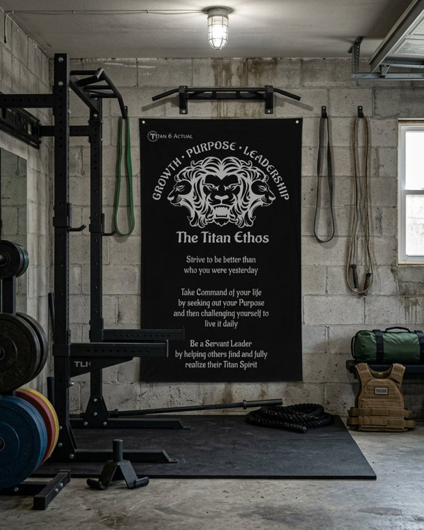 Titan 6 Actual "The Titan Ethos" Gym Banner featuring a multi-headed lion motif and motivational text, displayed on a cinder block wall in a garage gym with a power rack, barbell plates, and training gear.