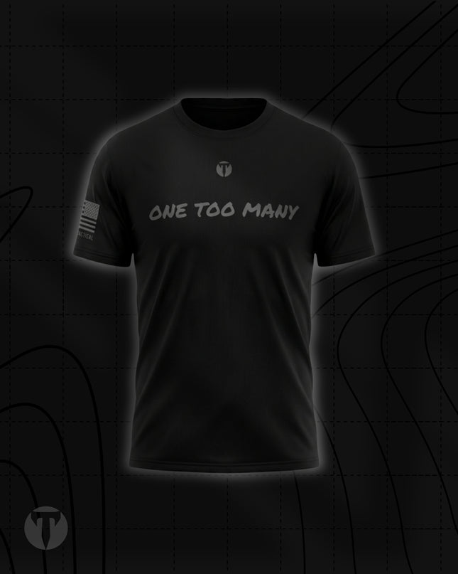 Front view of the Titan 6 Men's Endure T-Shirt in black, featuring the light grey chest graphic "ONE TOO MANY" below a small Titan 6 Icon logo and a monochromatic American flag graphic on the right sleeve.