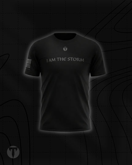 Front view of the Titan 6 Men's Endure T-Shirt in black, featuring the light grey chest graphic "I AM THE STORM" below a small Titan 6 Icon logo and a monochromatic American flag on the right sleeve.