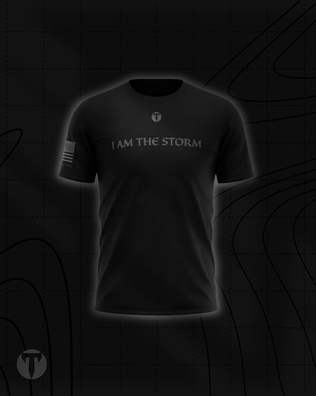 Front view of the Titan 6 Men's Endure T-Shirt in black, featuring the light grey chest graphic "I AM THE STORM" below a small Titan 6 Icon logo and a monochromatic American flag on the right sleeve.