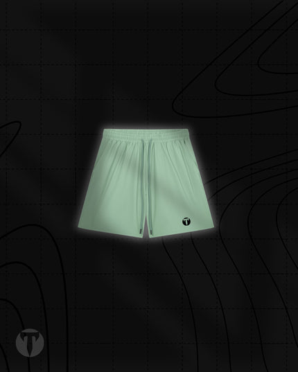 Front view of the Titan 6 Men's Stamina Drawstring Linerless Shorts in light sage green, featuring an elastic waistband with drawstrings and the dark Titan 6 Icon logo printed on the left leg hem.