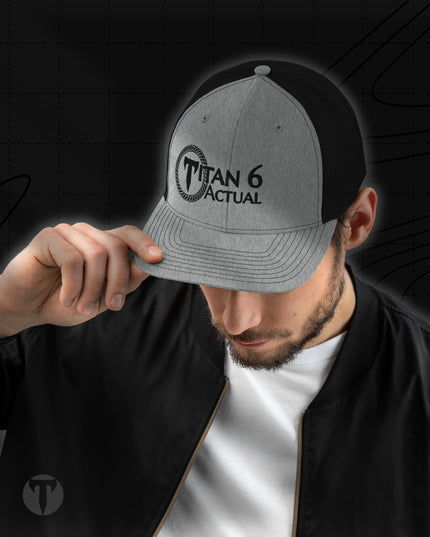 A man wearing a heather gray and black trucker cap with a black brim, holding the brim in front of his eyes. The cap features a black circular logo with the text 'TITAN 6 ACTUAL'.