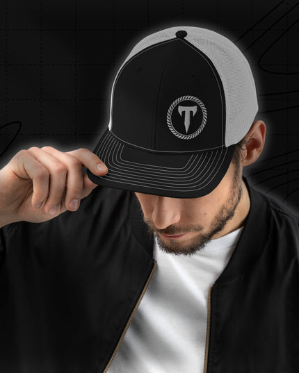 A man wearing a black jacket and the Titan 6 Richardson 112 Trucker Snapback Cap in Black and white, featuring a silver Titan 6 Elite logo embroidered on the front left panel.
