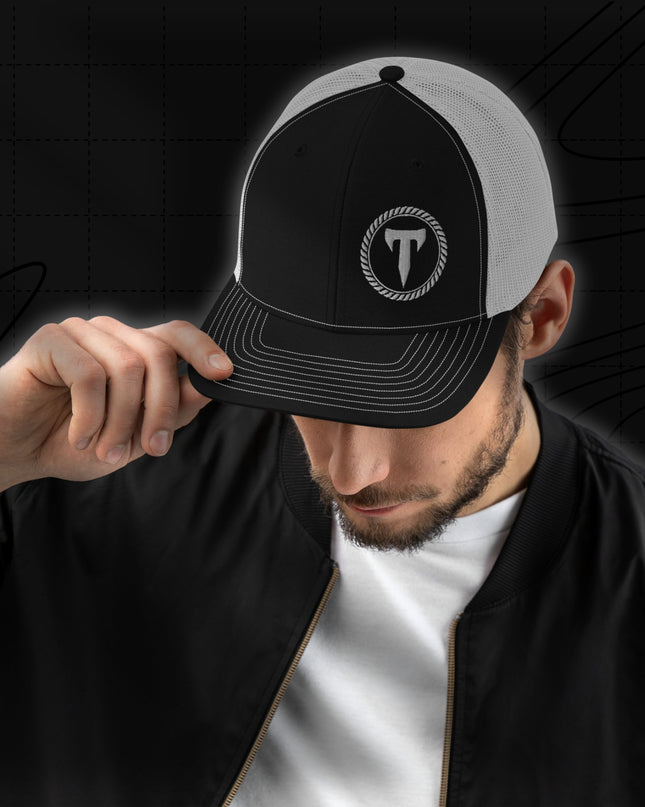 A man wearing a black jacket and the Titan 6 Richardson 112 Trucker Snapback Cap in Black and white, featuring a silver Titan 6 Elite logo embroidered on the front left panel.