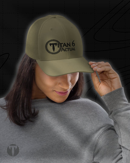 A woman wearing an olive green baseball cap with a black embroidered 'TITAN 6 ACTUAL' logo on the front, shown against a dark graphic background.