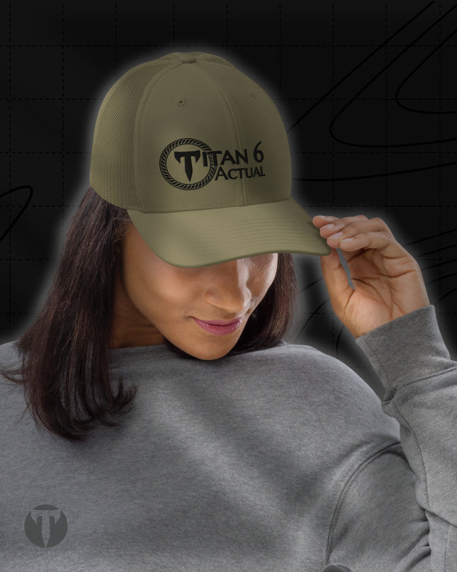 A woman wearing an olive green baseball cap with a black embroidered 'TITAN 6 ACTUAL' logo on the front, shown against a dark graphic background.