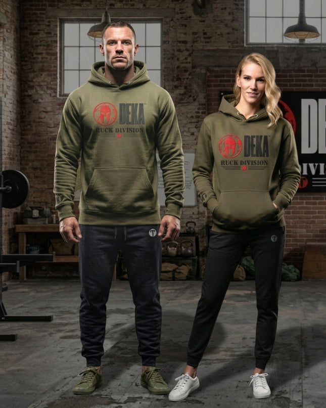 A man and a woman modeling matching olive green Titan 6 Citadel  hoodies with a red and black Spartan 'DEKA RUCK DIVISION' and red Titan 6 Icon logo on the chest, set in a rustic industrial loft with brick walls and gym equipment.
