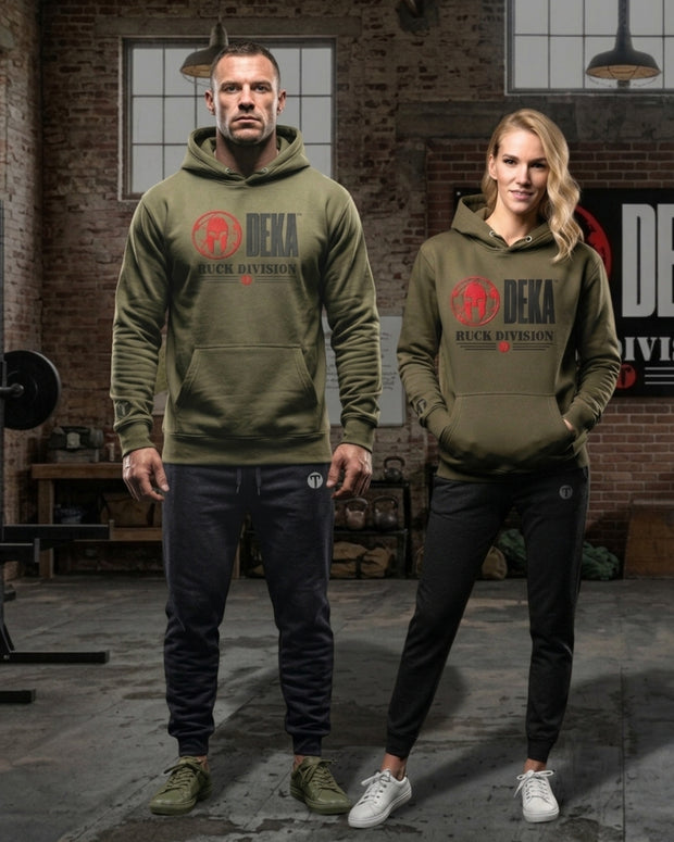 A man and a woman modeling matching olive green Titan 6 Citadel  hoodies with a red and black Spartan 'DEKA RUCK DIVISION' and red Titan 6 Icon logo on the chest, set in a rustic industrial loft with brick walls and gym equipment.