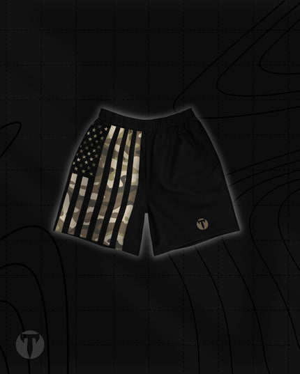 Front view of the Titan 6 Unisex Endure 6-Inch Linerless Shorts in Shadow Patriot, featuring a split design with a camouflage American flag print on the right leg, solid black on the left leg, and a bronze Titan 6 Icon logo on the left leg hem.
