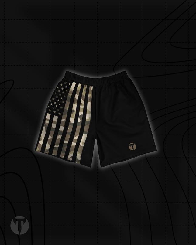 Front view of the Titan 6 Unisex Endure 6-Inch Linerless Shorts in Shadow Patriot, featuring a split design with a camouflage American flag print on the right leg, solid black on the left leg, and a bronze Titan 6 Icon logo on the left leg hem.