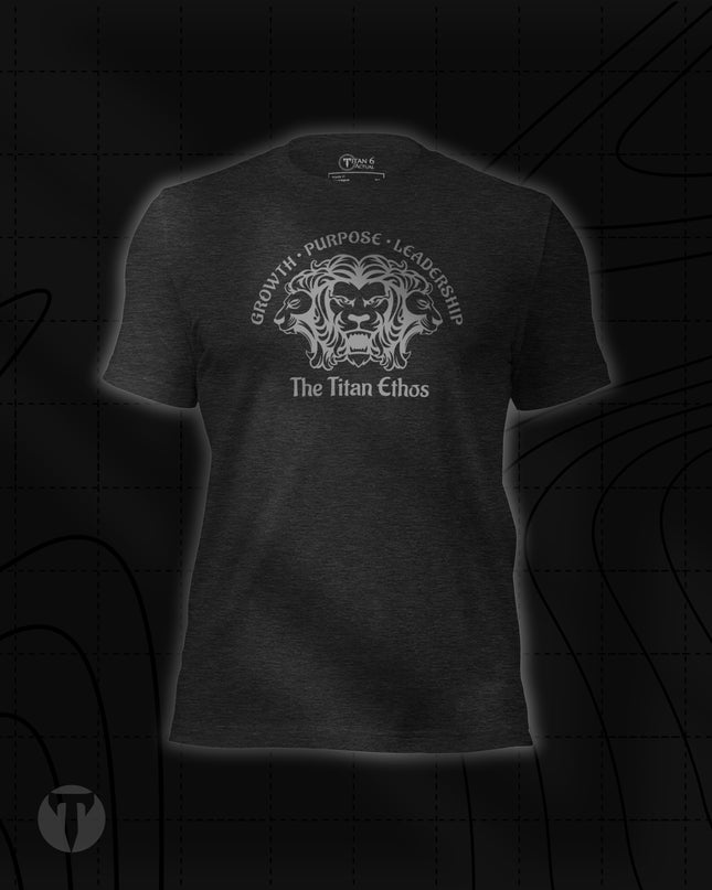 Titan 6 Unisex Nomad Tee in Dark Grey Heather, featuring a silver three-headed lion emblem with "GROWTH • PURPOSE • LEADERSHIP" arched above and "The Titan Ethos" printed below.