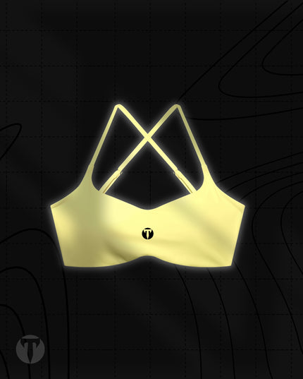 Front view of the Titan 6 Women's Apex Crop Sports Bra in soft yellow, featuring crisscross shoulder straps and the dark Titan 6 Icon logo centered on the chest.