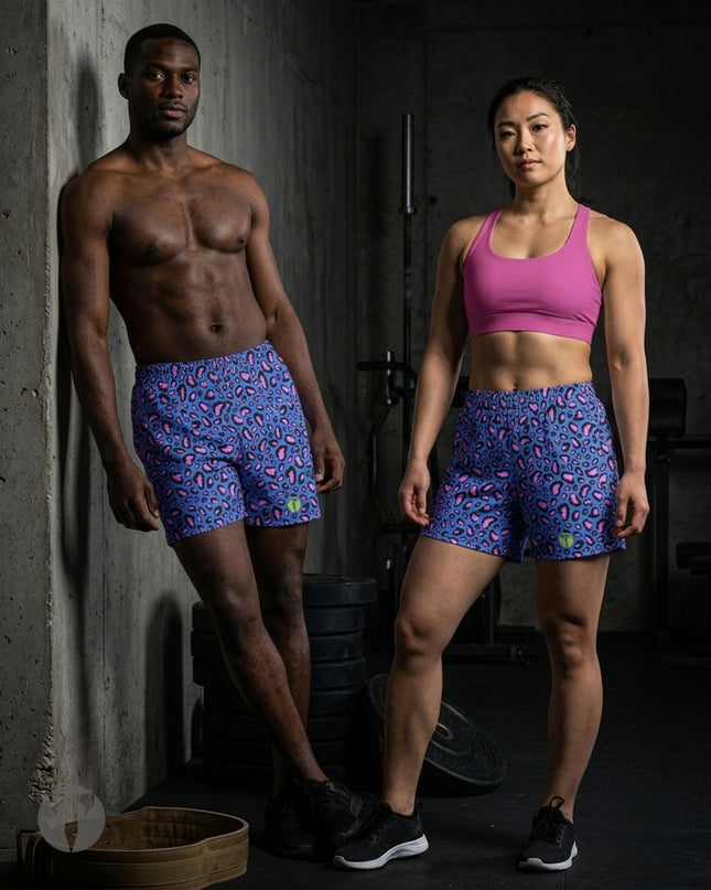 A shirtless man and a woman standing in a gym, both wearing matching Titan 6 Endure 6.5 inch linerless shorts in the Electric Leopard pattern. The woman is also wearing a pink sports bra, and the background shows dark gym equipment and a concrete wall.