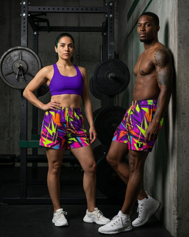 A man and a woman posing in a gym setting, both wearing matching Titan 6 Unisex Endure shorts in the famous Zack Wiz pattern with a vibrant, multicolored abstract pattern in purple, pink, yellow, green, and orange.